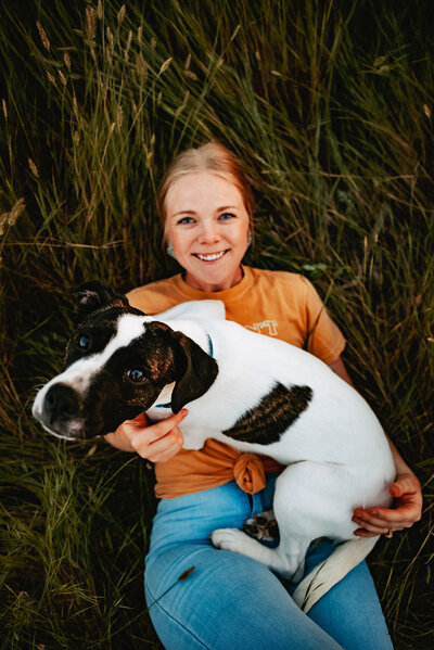 Woman laying down in grass with dog on lap looking up at the camera