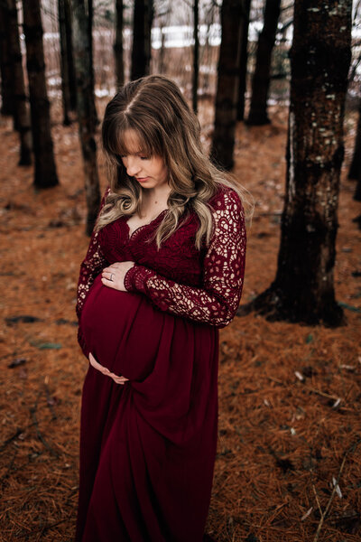 pregnant mom holding her baby belly wearing a burgundy dress