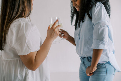 Two young women standing face to face with drinks in their hands.