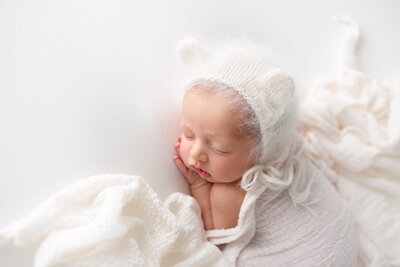 Newborn wearing a bear hat sleeping while being photographed