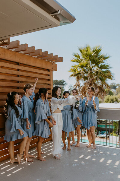 a bride pops champagne with her bridesmaids in matching pajamas