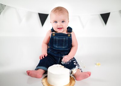 Baby boy smiles with cake during cake smash birthday session.