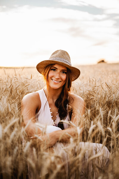 senior girl sits and smiles in wheat field in the summer