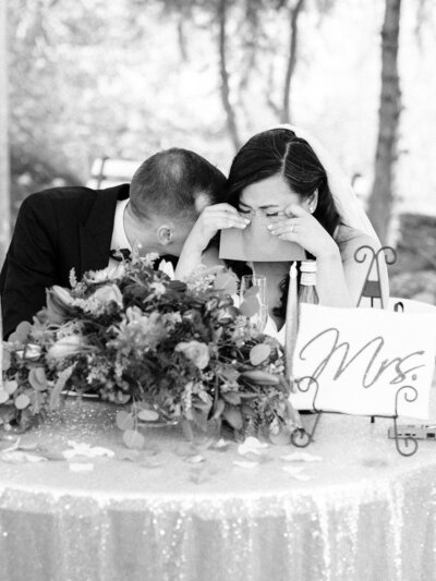 Bride and groom hide their faces as they cry during wedding toasts