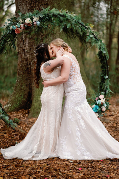 LGBTQ wedding with two brides sharing their first kiss at the altar after their vows have been said. Each bride is in her own wedding dress