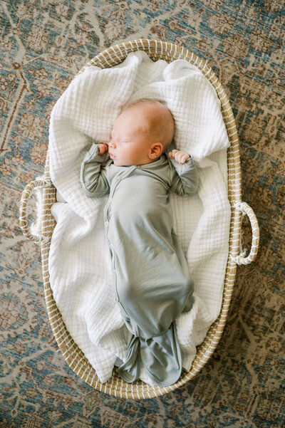 Newborn baby boy in green knotted gown sleeps in basket in raleigh newborn photography session