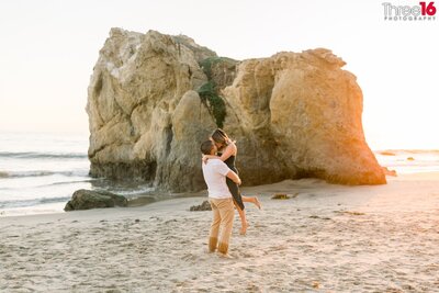 Groom to be whispers into his fiance's ear as they embrace each other on the sands of El Matador State Beach