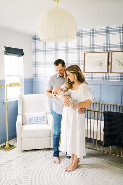New parents hold newborn baby boy in blue plaid nursery during newborn photography session.