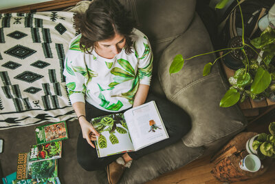 woman reads plant book on her sofa