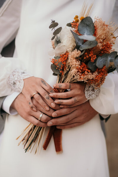 Das Hochzeitspaar hält gemeinsam beim Paarfotoshooting den Brautstrauß vor dem Bauch der Braut.