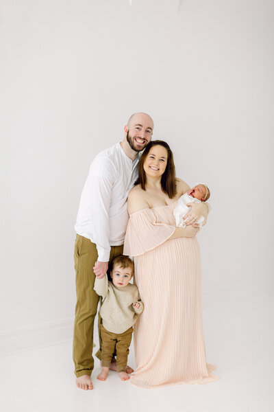 Mother holding newborn baby, father standing next to her holding their toddlers hand by Cincinnati Newborn Photographer
