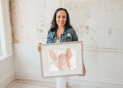 Photographer in a jean jacket displaying a framed photo of a baby