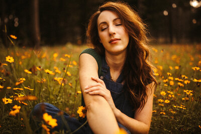 woman sitting in field of wild flowers with her eyes closed