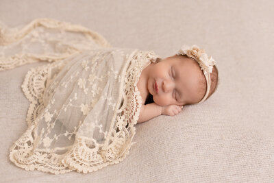 A newborn baby sleeping with a lace blanket on top of them.
