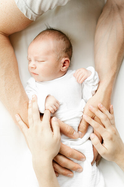 newborn baby in white onesie with hands on him