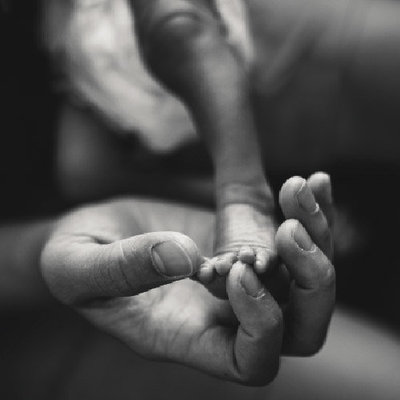 Black and white detail photo of adult hand holding tiny newborn foot.