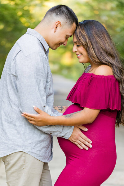 A couple touching foreheads and smiling while hugging mom’s pregnant belly at a photography session in Lorton, VA.
