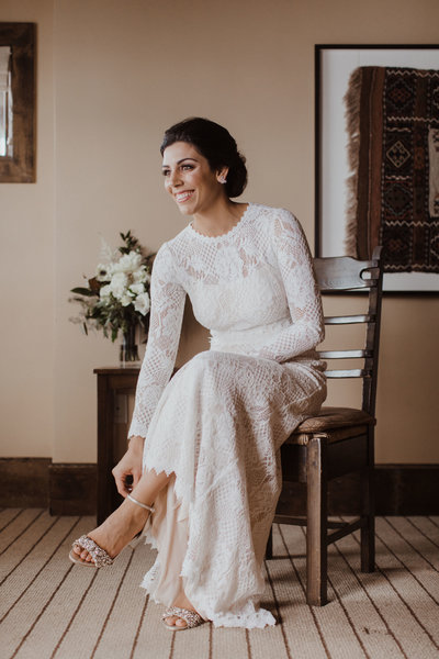 bride sitting on chair smiling and touching her shoe