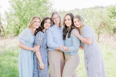 A mom and her daughters stand in a field for a photo huddled close together