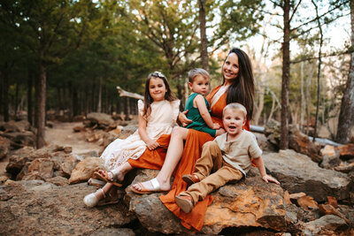 Mom Surrounded by three kids sitting on a rock smilinfg