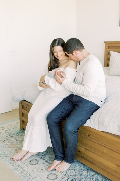 Husband cradles baby's head and kisses wife's shoulder during Austin newborn photography session.