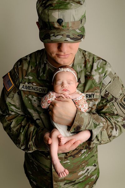 new dad dressed in his military fatigues holds his newborn daughter