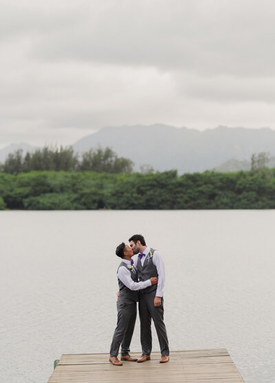 two grooms kiss on lake in hawaii for their multicultural destination wedding. lgbtq friendly.