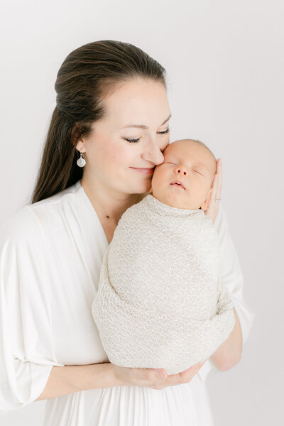 A DC Newborn Photography photo of a mother holding her newborn baby up close to her face and snuggling into him