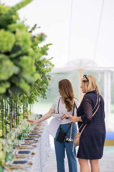 uxury party planner emma westacott and her team perfecting a dining table decorated with tall green flowers in a marquee