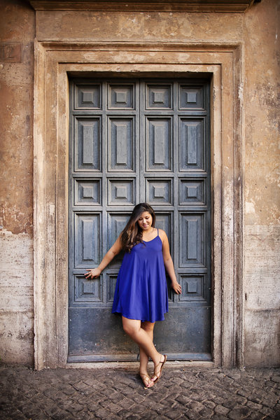 A girl in a blue dress in front of a grey door in Trastevere. Taken by Rome Vacation Photographer, Tricia Anne Photography