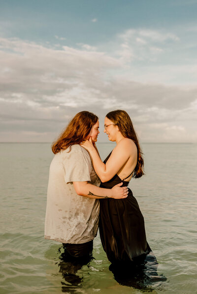 engaged lesbian couple stands embracing in water on panama city beach