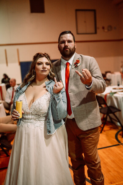 bride and groom holding their ring fingers up at wedding reception