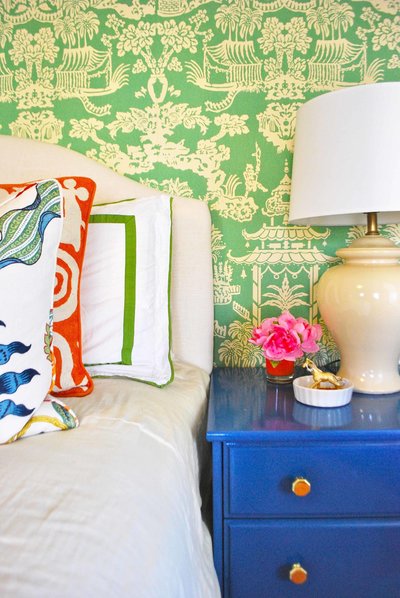 A bed and blue night stand in front of green wallpapered wall.