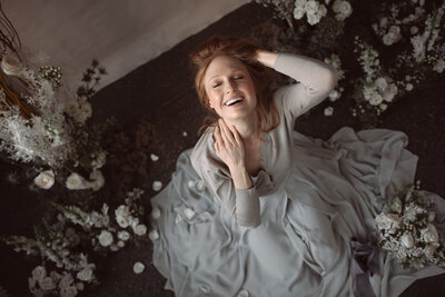 A happy bride in a gray wedding gown laughs as petals fall around her.