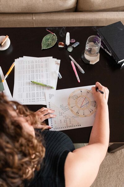 woman sitting at a table with pens and crystals on it writing on a piece of paper