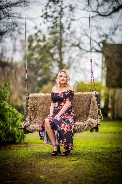 woman in a floral dress sits on an outdoor chair smiles for the camera