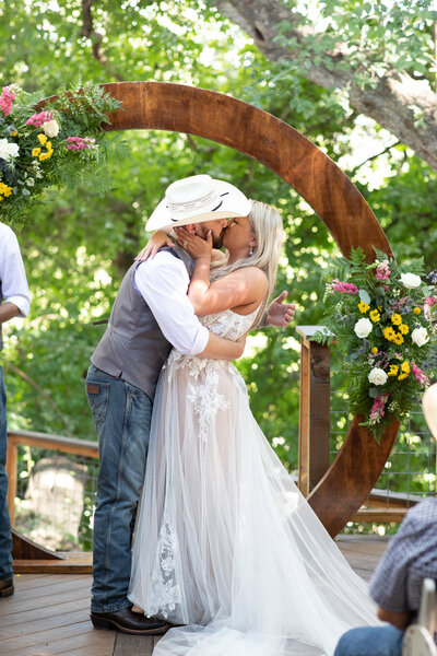 An Austin-based wedding photographer captures a bride and groom's intimate kiss beneath a beautiful wooden arch.