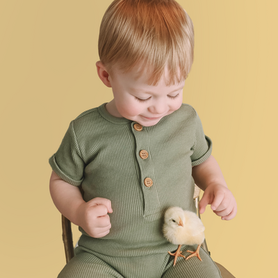Young boy wearing green looks down at a baby chick in his lap