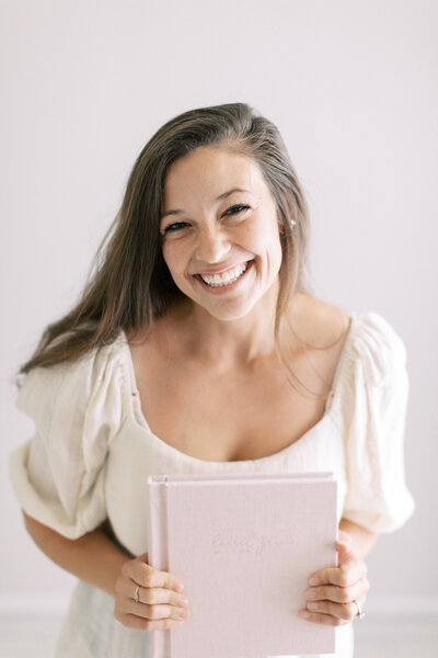 photo of madison wi newborn photographer, Talia Laird, the owner of Talia Laird Photography, holding a blush pink linen newborn album