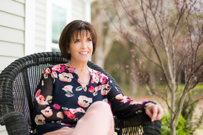 Realtor in a floral blouses poses for photo in a wicker chair
