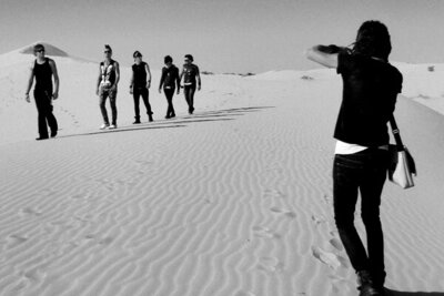 Behind the Scenes Band photoshoot Mark Maryanovich photographing My Darkest Days members as they walk in single file across sand dune black and white image