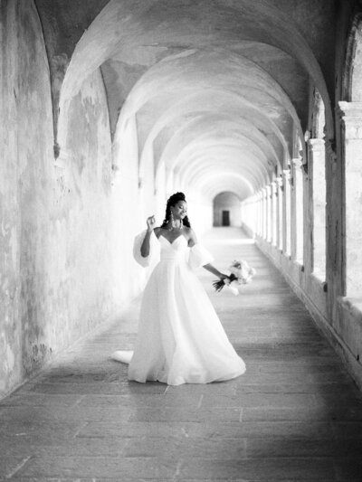 Bride strolls down arched hallway with wedding bouquet