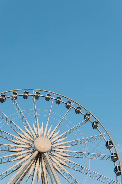 A close-up view of a Ferris wheel against a clear blue sky, showing its intricate metal framework and passenger gondolas.