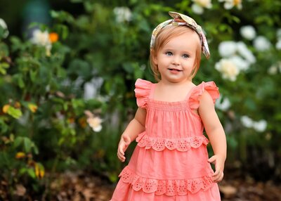 Cute girl in pink dress on posing in the flowers during her denver childrens portrait photography session.