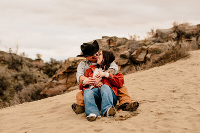 An engaged couple sits together on the sand dunes in Wenatchee, Washington.