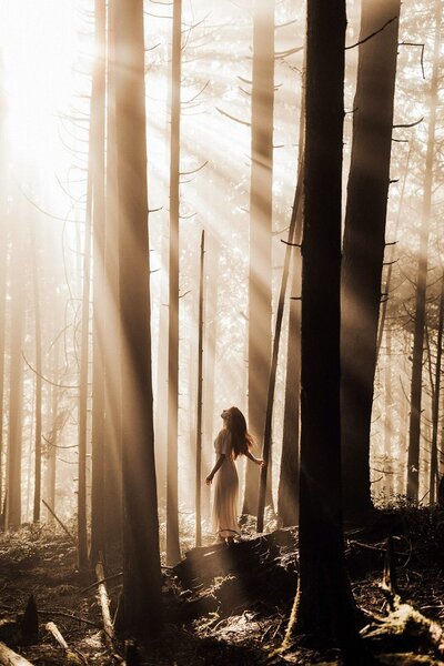 woman standing in forest with sun shining through trees