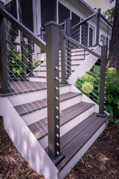 An L-shaped staircase using TimberTech Advanced PVC and contrasting white risers with aluminum cable railing. 