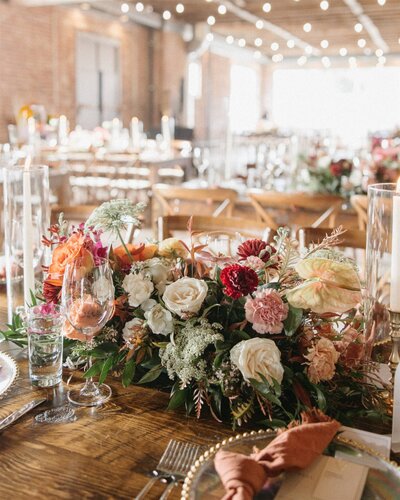 wedding reception table decorated with colorful florals, glassware and peach napkins