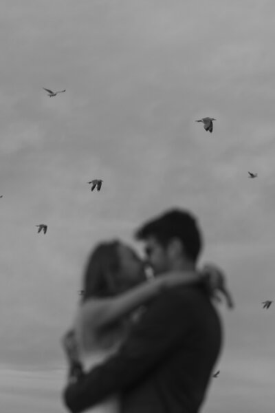 couple embrace with birds flying in the background 