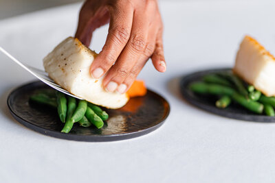 Chilean seabass being plated on top of green beans